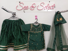 Green traditional outfit with gold embroidery on a white wall with 'See & Select' sign.